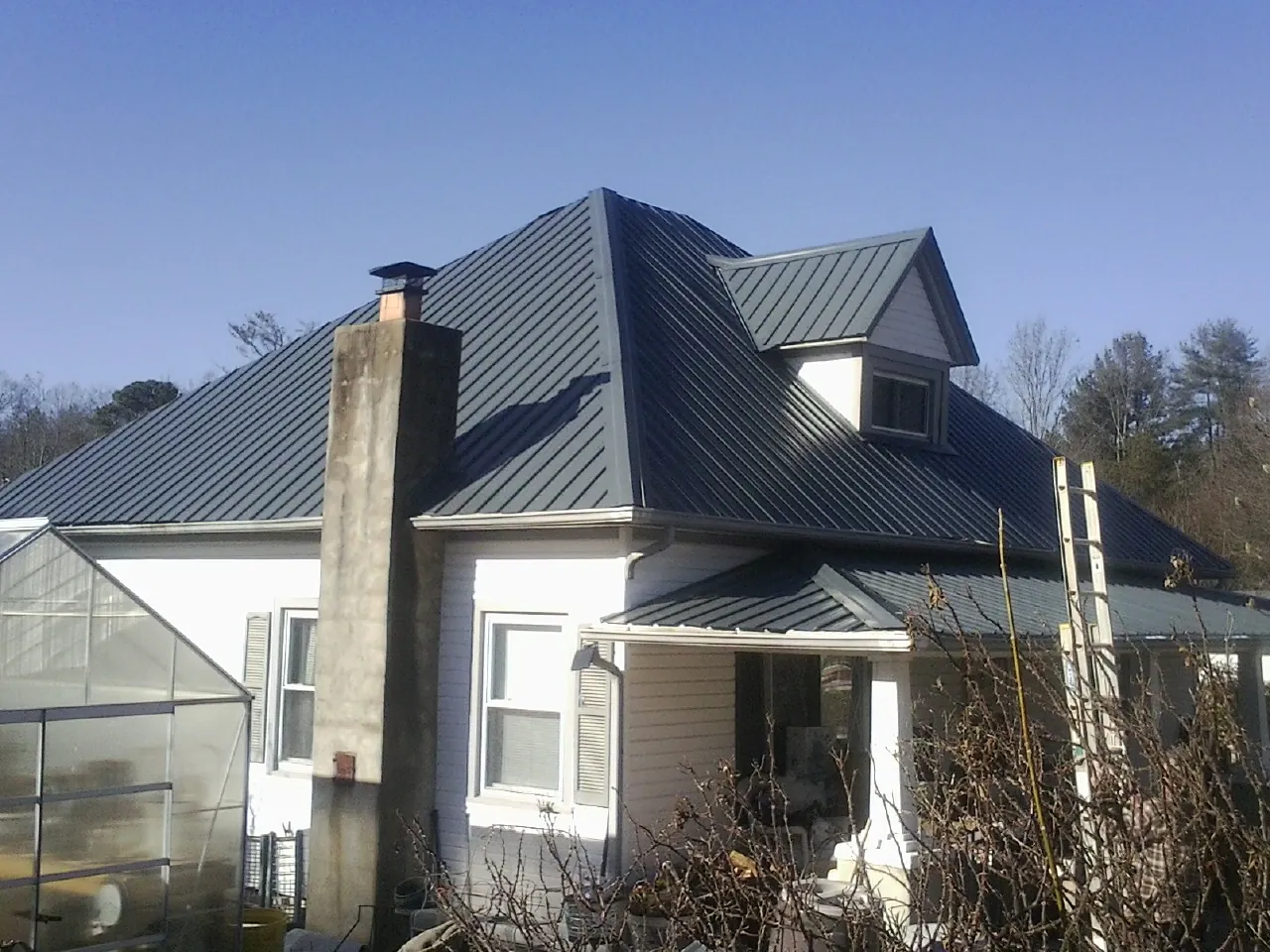 Dark blue standing seam metal roof on a white farmhouse with dormer — Slate & Tile Roof Repair by Roofing Brothers in Yaphank
