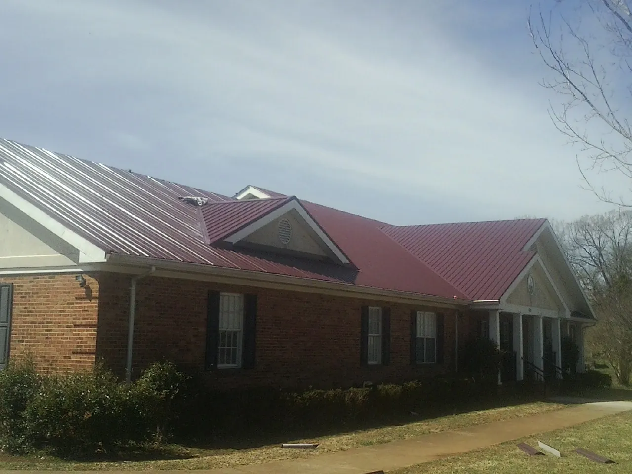 Red metal roof with gabled entries on a long brick building, from a Hail Damage Roof Repair job in Yaphank