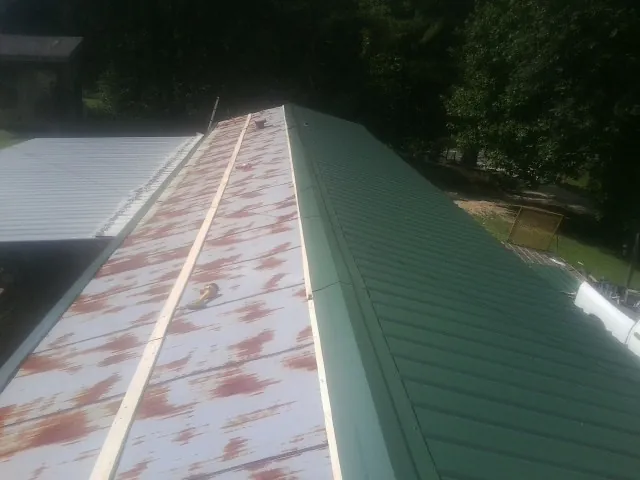 Old rusted panels beside newly installed green metal roofing — Wind Damage Roof Repair by Roofing Brothers in Yaphank