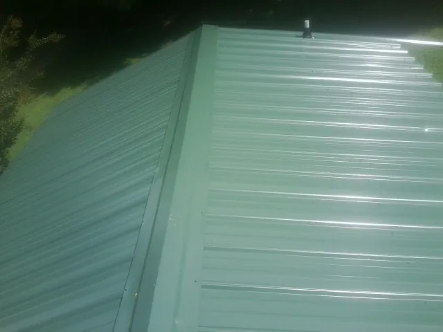 New green metal panels meeting at the ridge of a roof — Flat Roof Repair work by our crew in Yaphank