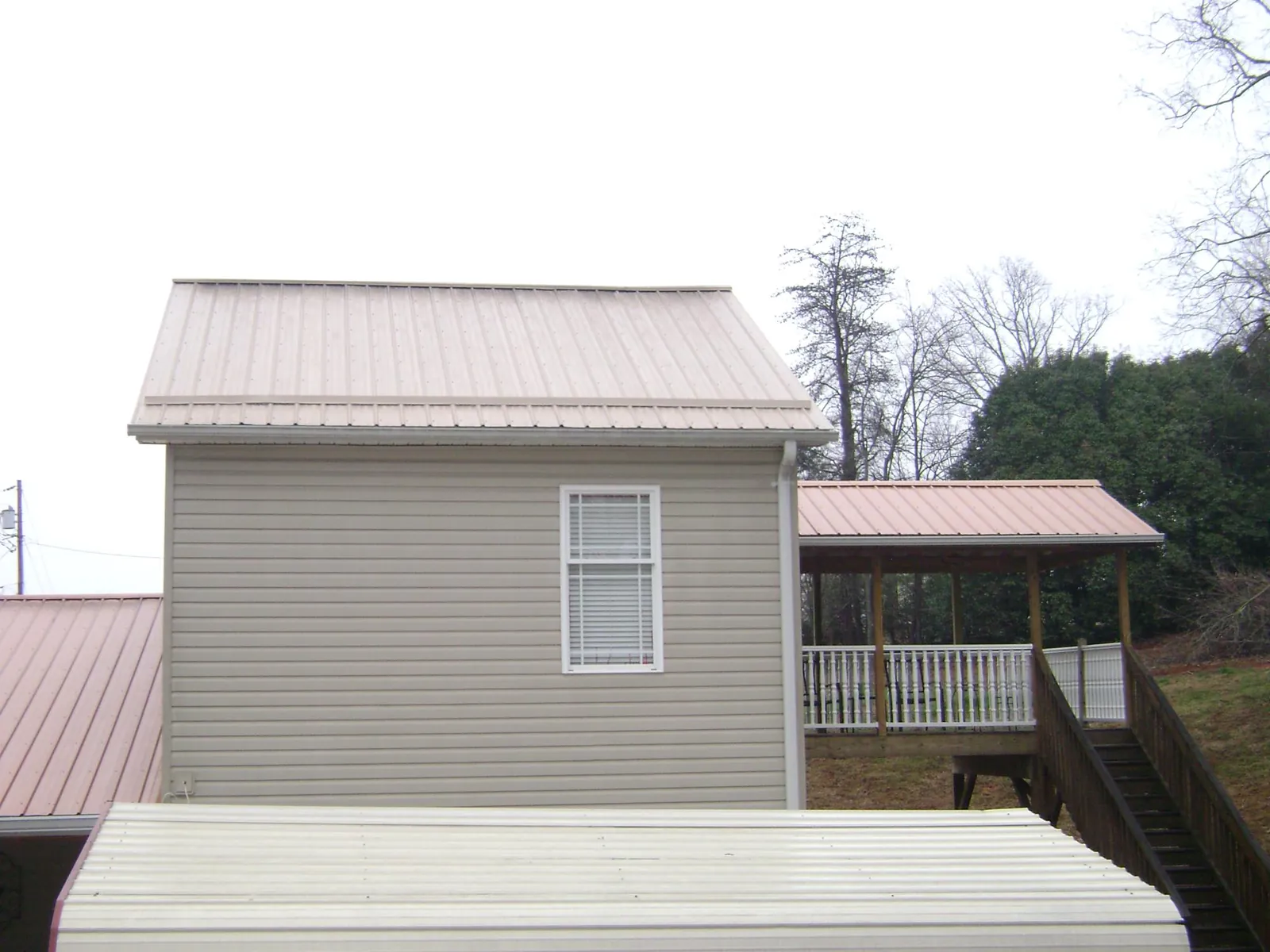 Tan metal roofs on a two story addition and attached porch, from a Roof Replacement job in Yaphank